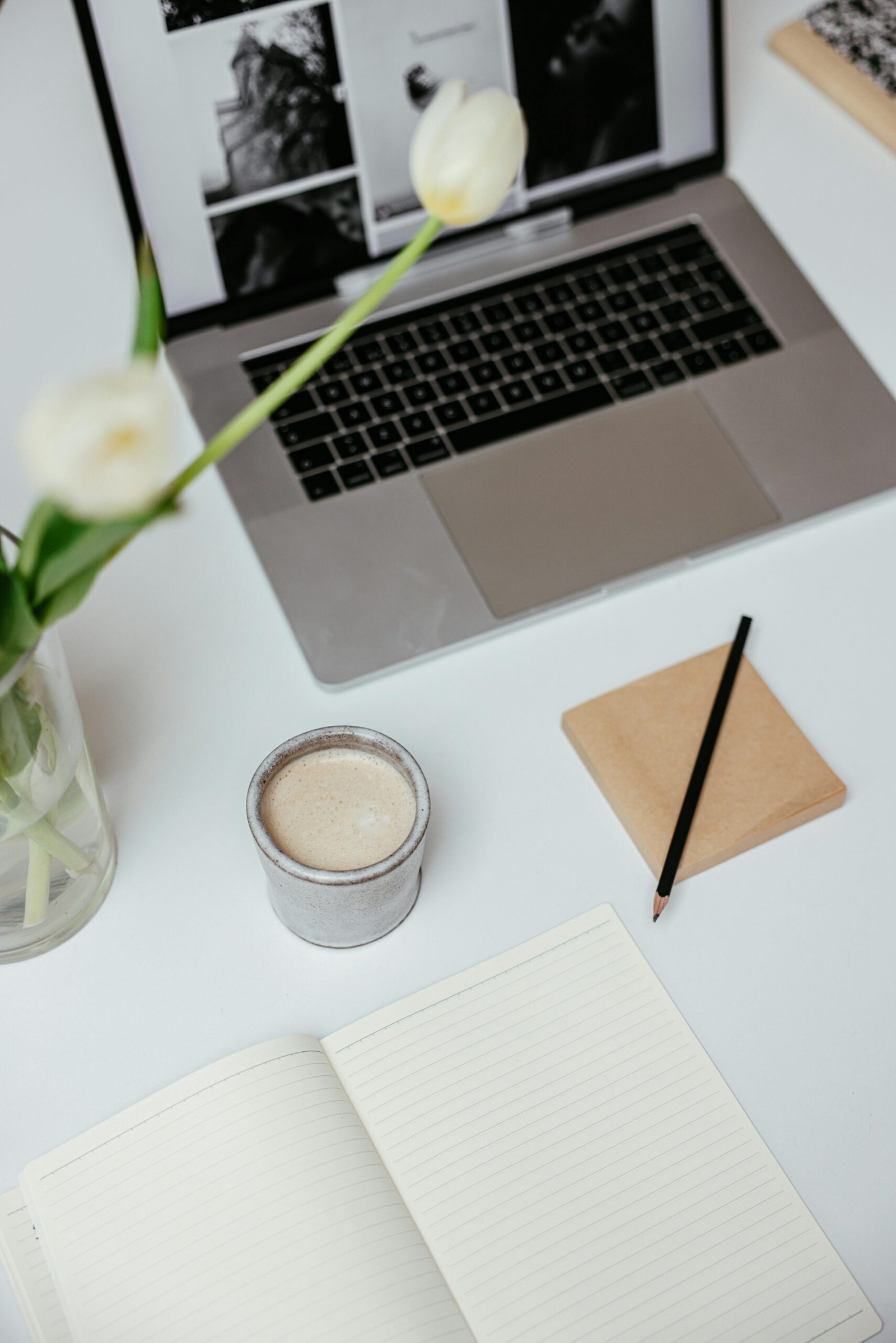 pexels-photo-7657399-7657399 Stylish workspace featuring laptop, coffee, tulips, and notebook on a white desk.